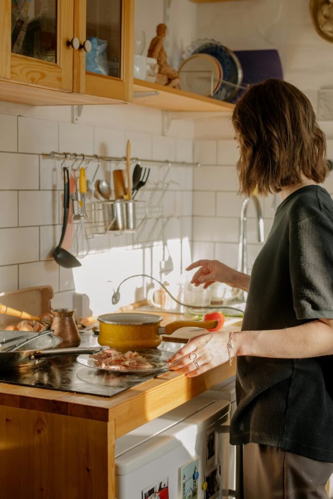 oil-1 A woman cooks breakfast in a sunlit kitchen, featuring bacon and kitchenware.